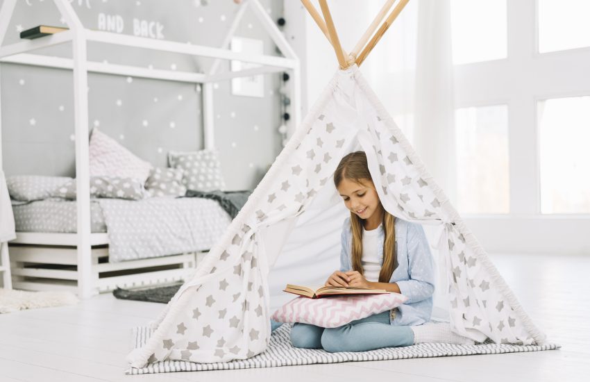 Łóżeczko dziecięce domek znajdujące się w tle pokoju w którym bawi się dziewczynka