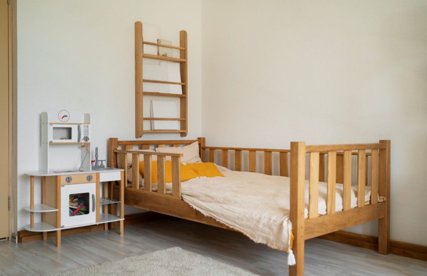 Łóżka dziecięce 140x70 z pionowymi szczebelkami pełniącymi funkcję barierki ochronnej. Łóżko jest zasłane jasną pościelą z żółtymi poduszkami dekoracyjnymi