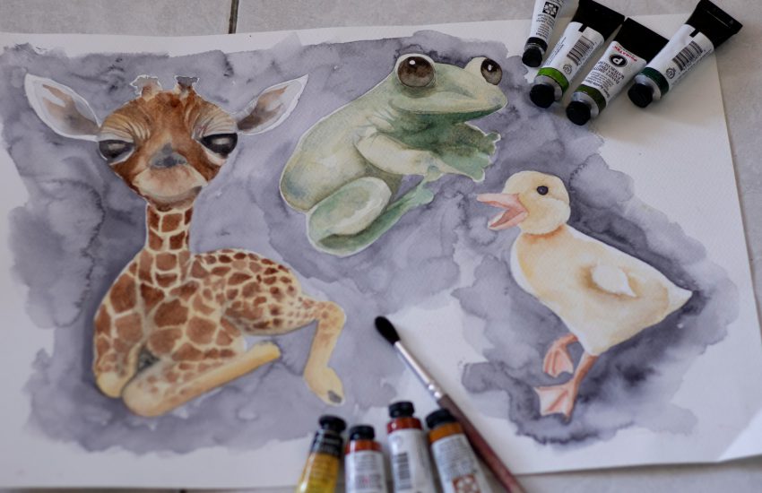Na obrazie widać akwarelową ilustrację trzech zwierząt: małej żyrafy, zielonej żabki i żółtego kaczątka