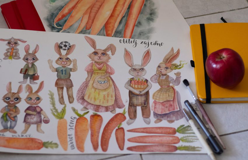 Na zdjęciu widać arkusz z akwarelowymi ilustracjami przedstawiającymi rodzinę królików oraz marchewki