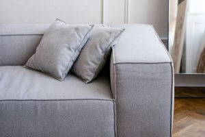 Zbliżenie na szary tapczan z funkcją spania o minimalistycznym designie, z dwiema dekoracyjnymi poduszkami na tle jasnej ściany