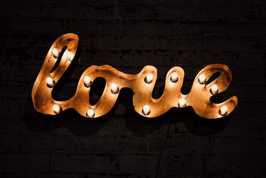 Na ciemnej, ceglanej ścianie widoczny jest podświetlany napis „love”